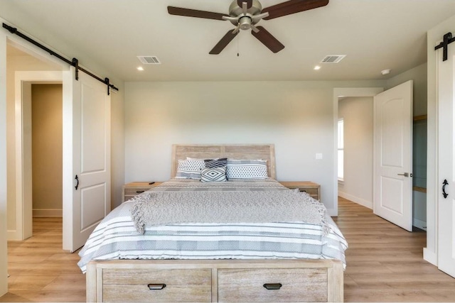 bedroom with a barn door, ceiling fan, and light hardwood / wood-style floors