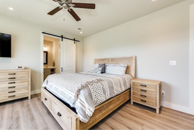 bedroom with light wood-type flooring, a barn door, ensuite bathroom, and ceiling fan