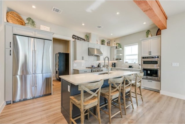 kitchen with a kitchen island with sink, light hardwood / wood-style flooring, white cabinetry, stainless steel appliances, and extractor fan