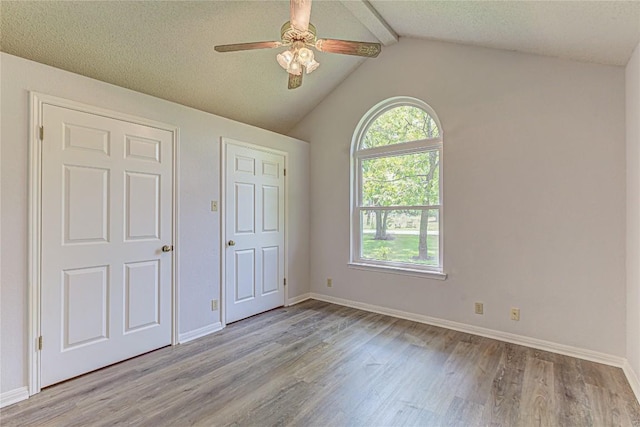 unfurnished bedroom featuring light wood-type flooring, a textured ceiling, lofted ceiling with beams, and ceiling fan