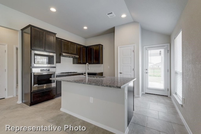 kitchen featuring light stone countertops, sink, stainless steel appliances, lofted ceiling, and a center island with sink