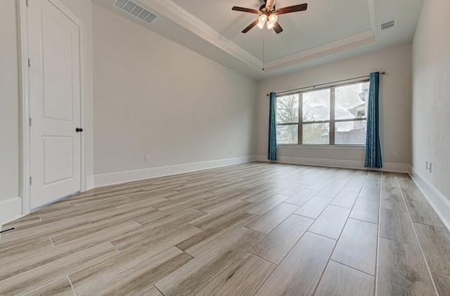 empty room featuring a raised ceiling, ceiling fan, crown molding, and light wood-type flooring