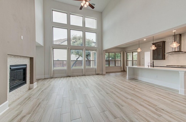 unfurnished living room with ceiling fan, light hardwood / wood-style floors, and a high ceiling