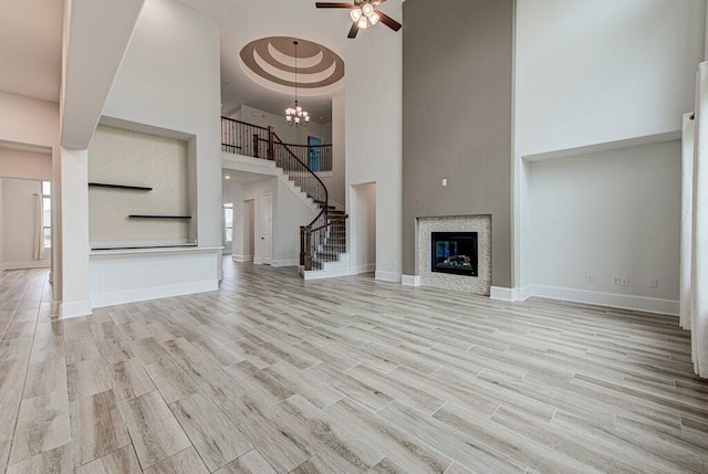 unfurnished living room with ceiling fan with notable chandelier, light hardwood / wood-style floors, and a towering ceiling