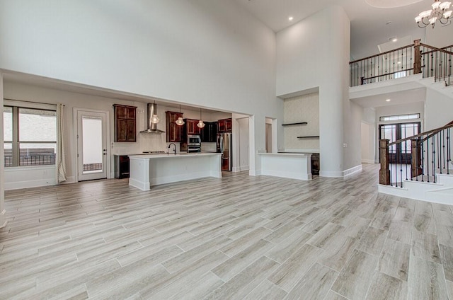 unfurnished living room with a notable chandelier, light hardwood / wood-style flooring, a high ceiling, and sink