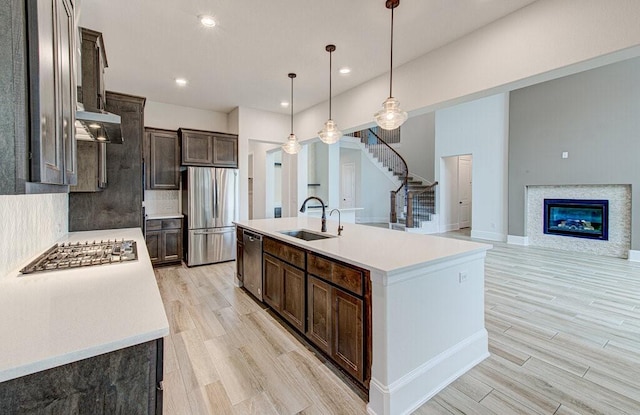 kitchen featuring sink, hanging light fixtures, stainless steel appliances, light hardwood / wood-style flooring, and an island with sink