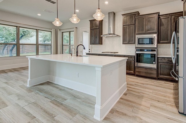 kitchen with pendant lighting, wall chimney range hood, sink, tasteful backsplash, and stainless steel appliances