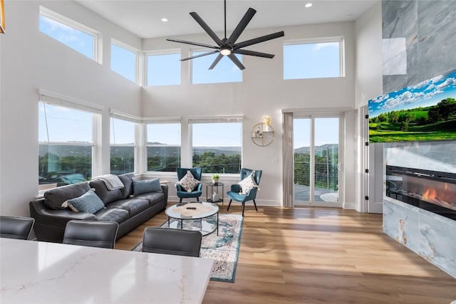 living room featuring a tile fireplace, a towering ceiling, light wood-type flooring, and ceiling fan