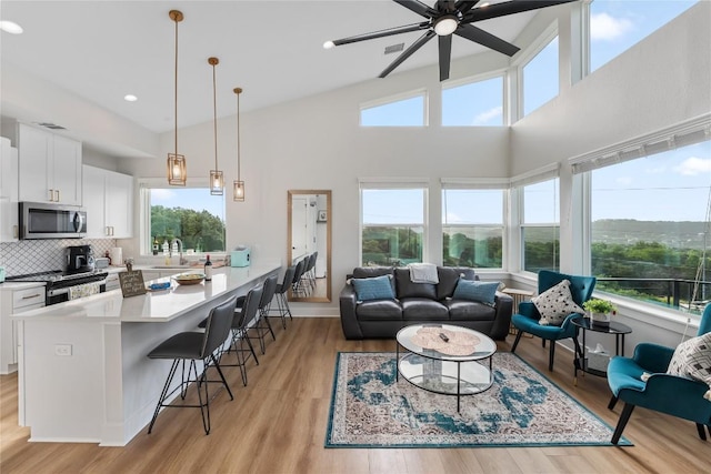 living room with high vaulted ceiling, light hardwood / wood-style flooring, ceiling fan, and sink