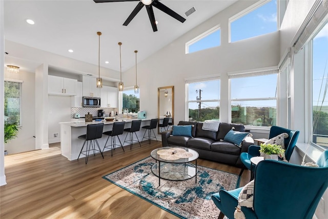 living room with ceiling fan, plenty of natural light, high vaulted ceiling, and light hardwood / wood-style flooring