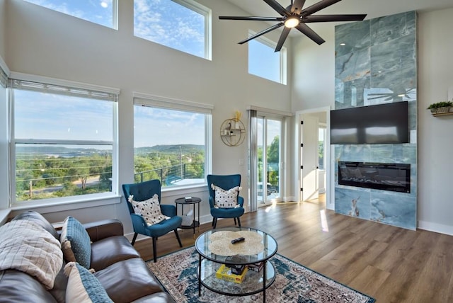 living room featuring ceiling fan, a fireplace, a towering ceiling, and hardwood / wood-style floors