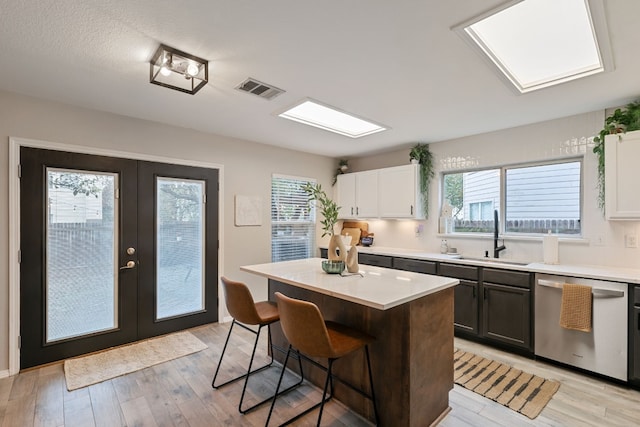 kitchen featuring sink, white cabinets, stainless steel dishwasher, light hardwood / wood-style floors, and a kitchen island