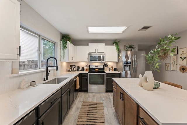 kitchen featuring white cabinetry, sink, light stone counters, light hardwood / wood-style floors, and appliances with stainless steel finishes