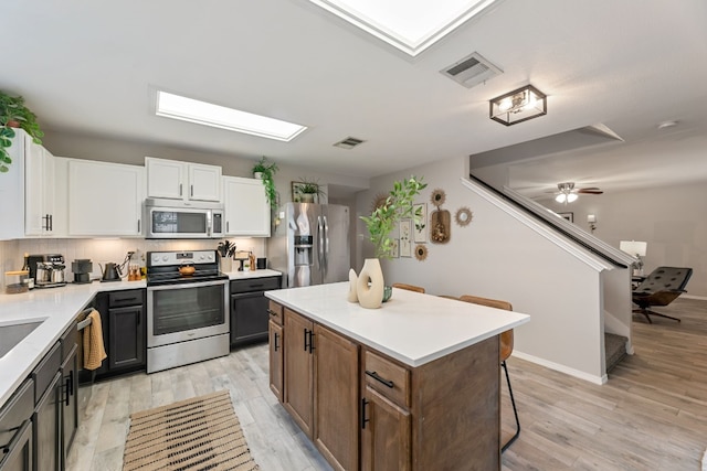 kitchen with backsplash, stainless steel appliances, white cabinets, a center island, and light hardwood / wood-style floors