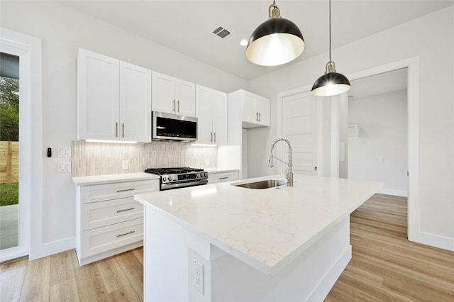 kitchen featuring a kitchen island with sink, hanging light fixtures, sink, appliances with stainless steel finishes, and white cabinetry