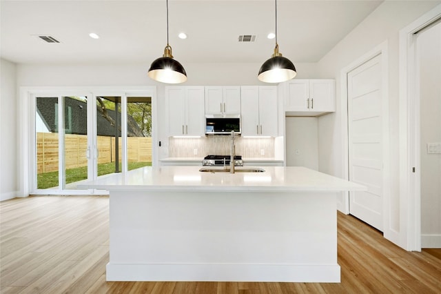 kitchen featuring decorative backsplash, a center island with sink, white cabinetry, and hanging light fixtures