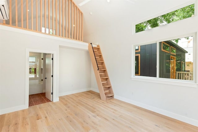 unfurnished room featuring wood-type flooring, a towering ceiling, and a wall unit AC