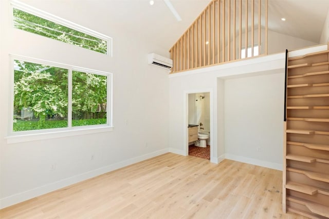 empty room featuring high vaulted ceiling, a wall mounted air conditioner, and light wood-type flooring