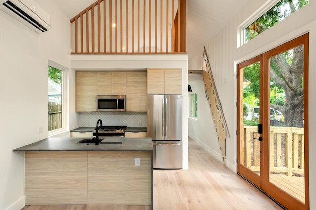 kitchen with a wall mounted air conditioner, light wood-type flooring, kitchen peninsula, and appliances with stainless steel finishes