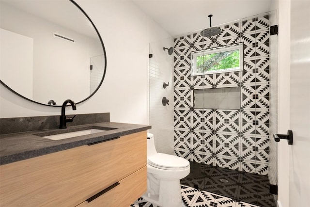 bathroom with tiled shower, vanity, toilet, and tile patterned flooring