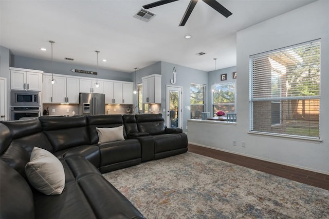 living area with dark wood-style flooring, visible vents, baseboards, and a ceiling fan