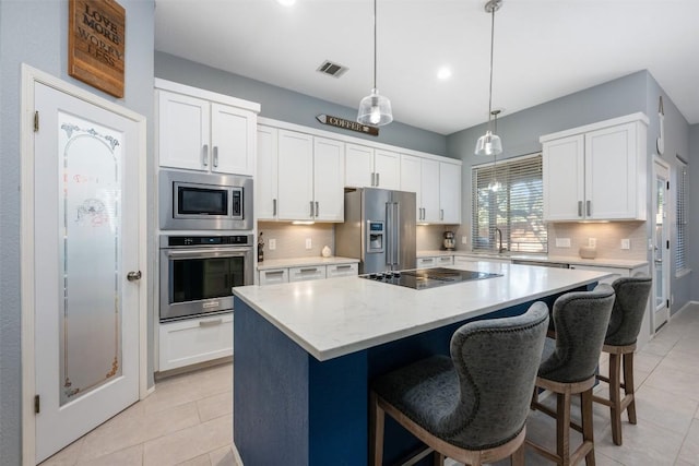 kitchen featuring tasteful backsplash, white cabinetry, stainless steel appliances, a kitchen island, and light tile patterned flooring