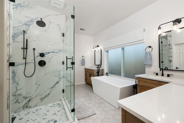 full bathroom with two vanities, a marble finish shower, visible vents, a freestanding bath, and a sink
