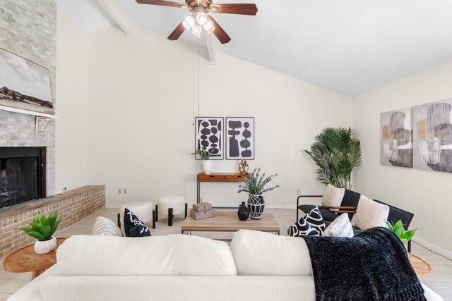 living room featuring vaulted ceiling with beams, light hardwood / wood-style floors, a brick fireplace, and ceiling fan