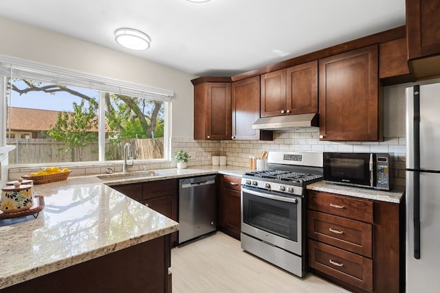 kitchen with light stone countertops, decorative backsplash, stainless steel appliances, sink, and light hardwood / wood-style flooring