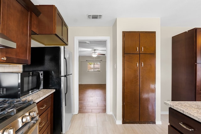 kitchen with ceiling fan, light wood-type flooring, appliances with stainless steel finishes, tasteful backsplash, and light stone counters