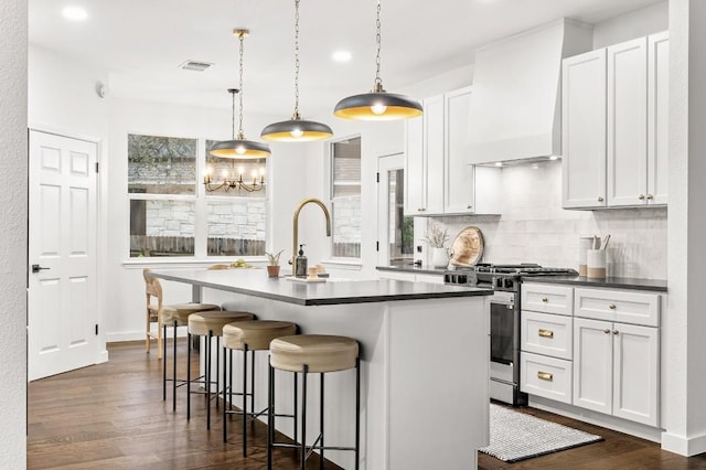 kitchen with gas range, white cabinetry, a kitchen island with sink, and custom range hood