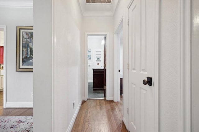 hall with ornamental molding, wood finished floors, visible vents, and baseboards