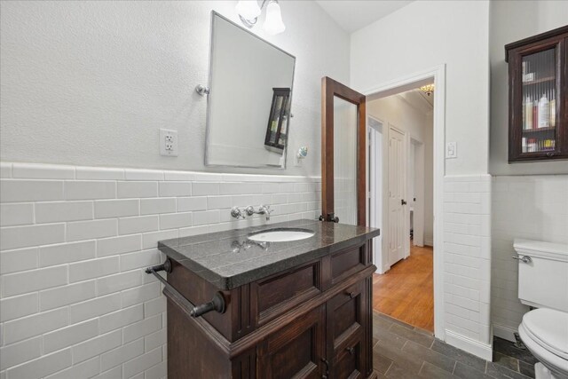 bathroom with a wainscoted wall, tile walls, toilet, and vanity