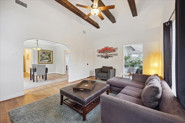 living room featuring arched walkways, beam ceiling, visible vents, and light wood-style flooring