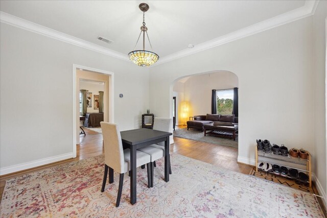 dining area with arched walkways, visible vents, crown molding, and light wood finished floors