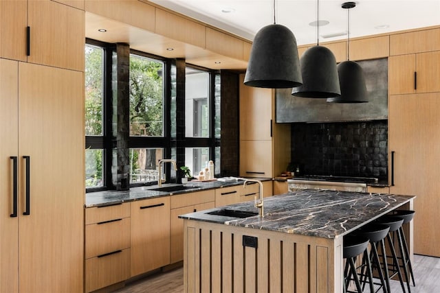 kitchen with sink, decorative light fixtures, a center island with sink, dark stone countertops, and a breakfast bar area