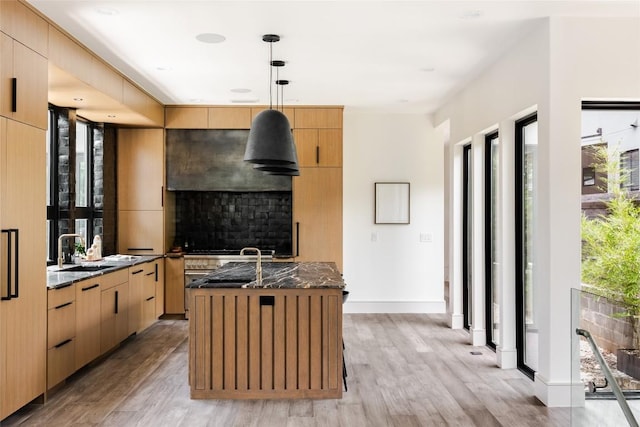 kitchen featuring light hardwood / wood-style floors, hanging light fixtures, dark stone counters, and sink