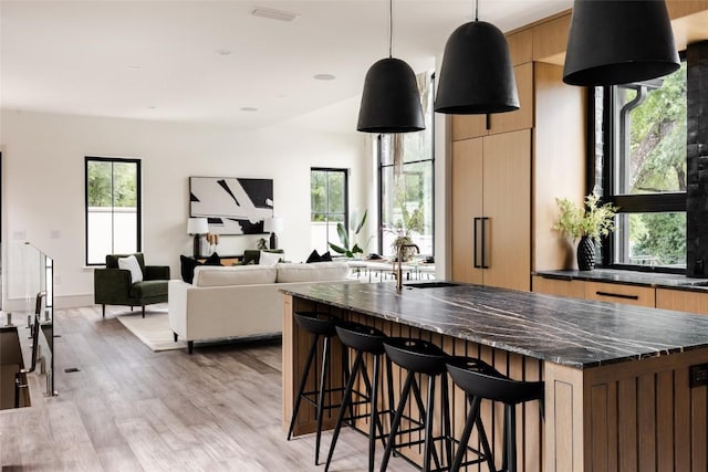 kitchen with a kitchen bar, light wood-type flooring, dark stone counters, sink, and pendant lighting