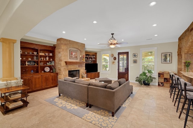 living room featuring a stone fireplace, ceiling fan, and crown molding