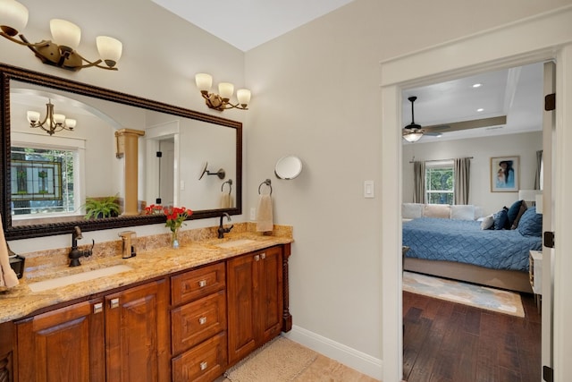 bathroom featuring vanity, wood-type flooring, ceiling fan with notable chandelier, and a raised ceiling