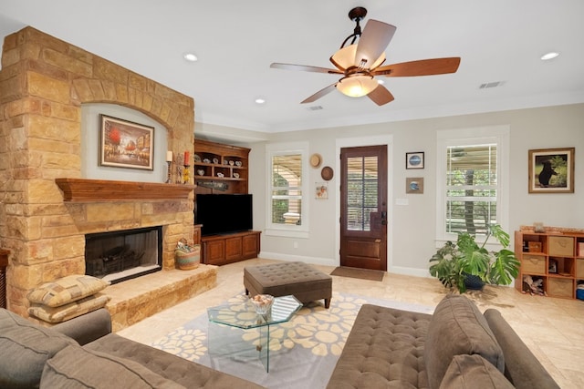 tiled living room with ceiling fan, a healthy amount of sunlight, ornamental molding, and a fireplace