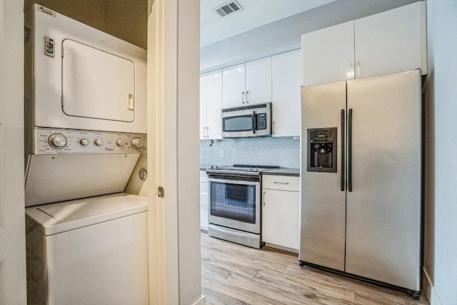 6444 Burnet Rd Unit 305, Austin, TX 78757 - kitchen featuring stainless steel appliances, stacked washer and clothes dryer, white cabinetry, and light wood-style flooring