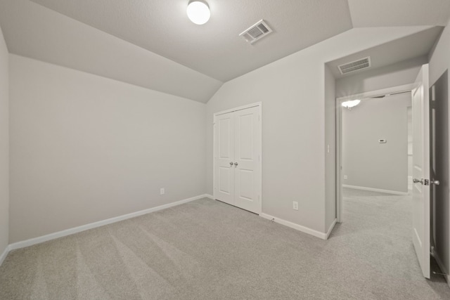 unfurnished bedroom with light carpet, a closet, and lofted ceiling