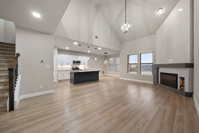 unfurnished living room with a chandelier, sink, high vaulted ceiling, and light hardwood / wood-style flooring