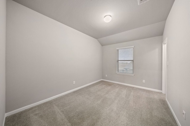 empty room with a textured ceiling, lofted ceiling, and carpet floors