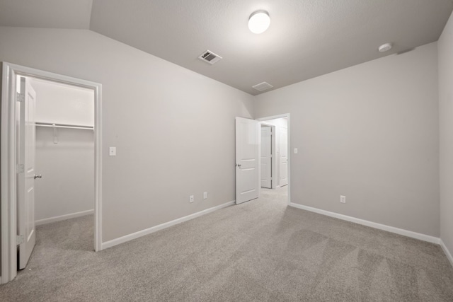 unfurnished bedroom featuring light carpet, a walk in closet, vaulted ceiling, and a closet