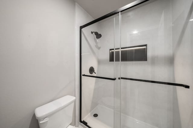 bathroom featuring a shower with door and toilet