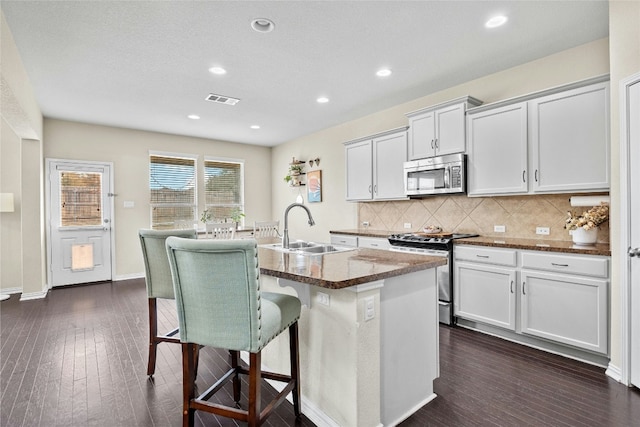 kitchen with dark hardwood / wood-style flooring, stainless steel appliances, sink, a center island with sink, and white cabinets