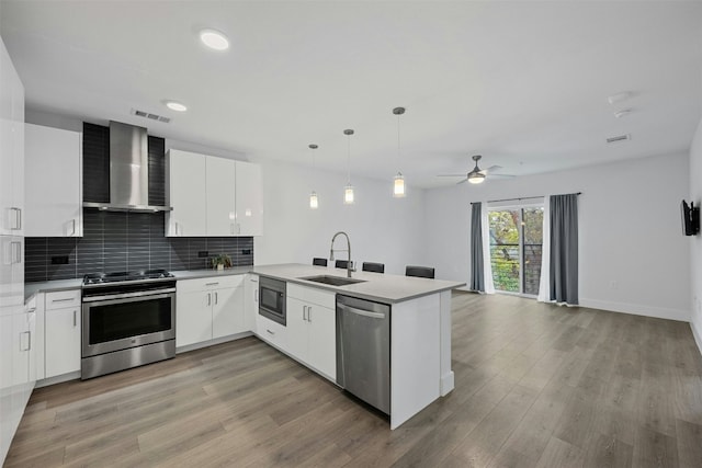 kitchen with kitchen peninsula, appliances with stainless steel finishes, decorative light fixtures, and wall chimney range hood