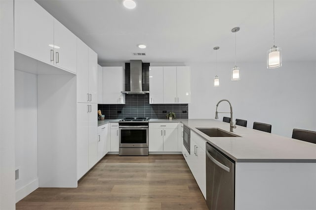 kitchen featuring appliances with stainless steel finishes, wall chimney exhaust hood, sink, pendant lighting, and white cabinetry